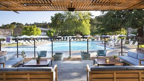 A poolside area with lounge chairs, a wooden pergola, and a view of a swimming pool.