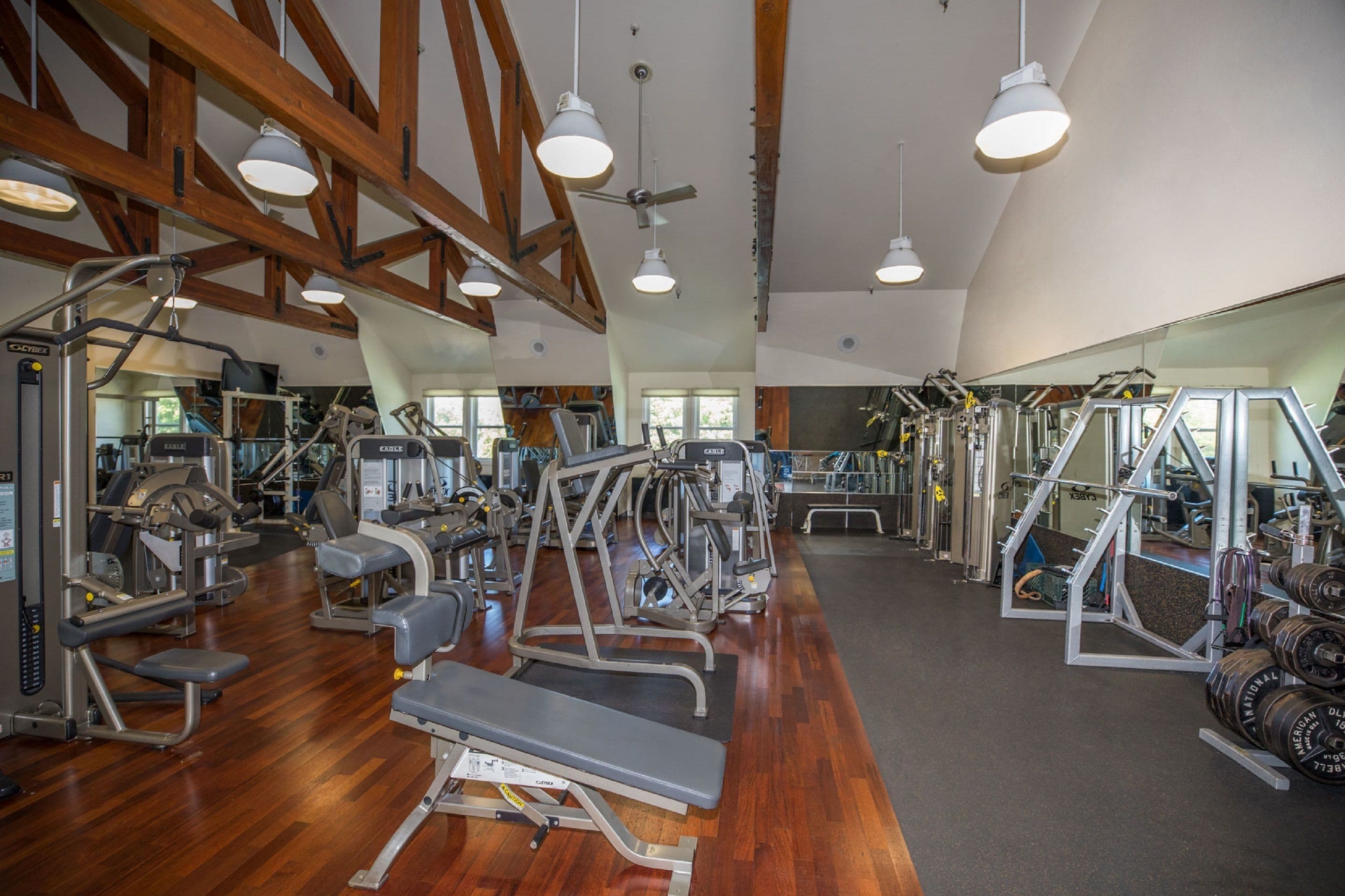 A gym with various exercise equipment, wooden beams on the ceiling, and large windows.