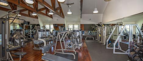 A gym with various exercise equipment, wooden beams on the ceiling, and large windows.