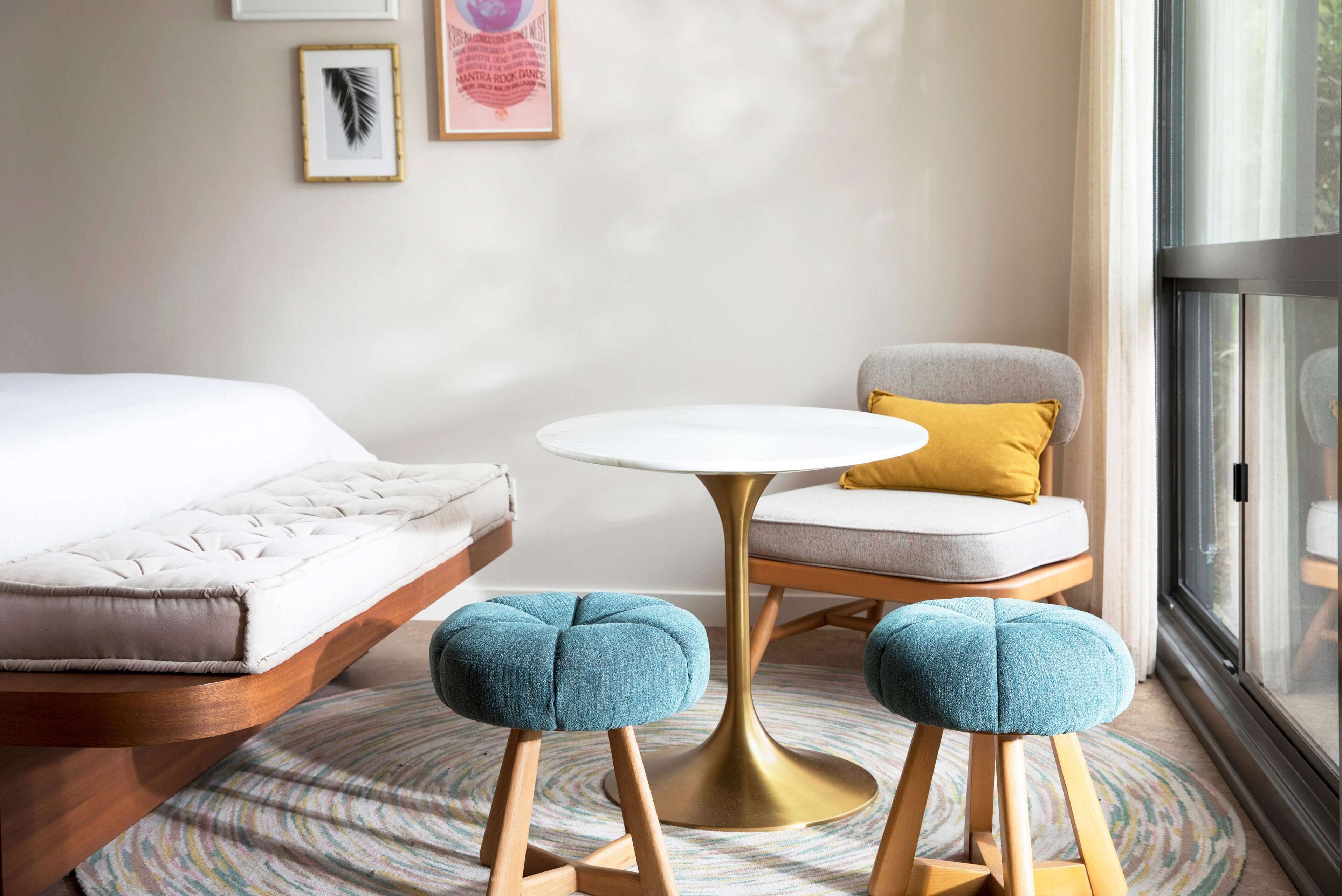 Una habitación de hotel moderna con una cama, una mesita pequeña y redonda, una silla y dos otomanas.