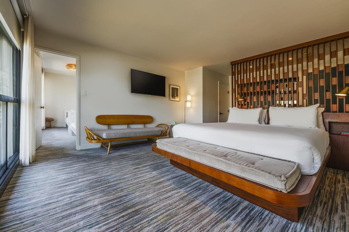 Habitación de hotel moderna con una cama grande, un sofá, un televisor y un panel decorativo en la pared.