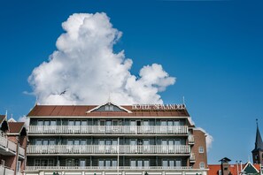 A multi-story hotel with a prominent balcony on the second floor, a large cloud in the sky, and a bird flying near the top.