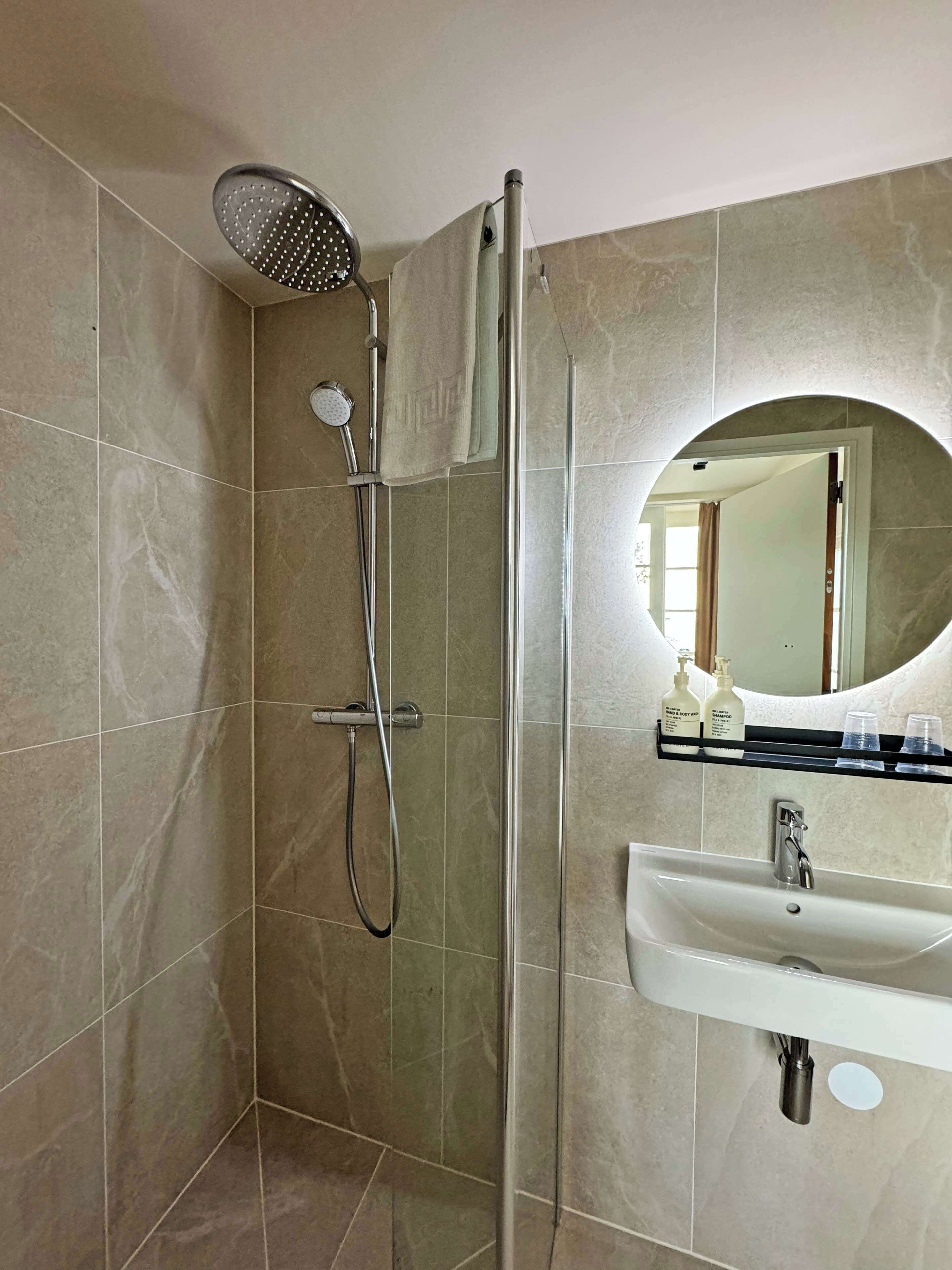A bathroom with a glass-enclosed shower, a sink, and a mirror.