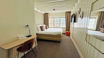 A hotel room with a bed, a desk, a chair, a mirror, and a window with curtains.