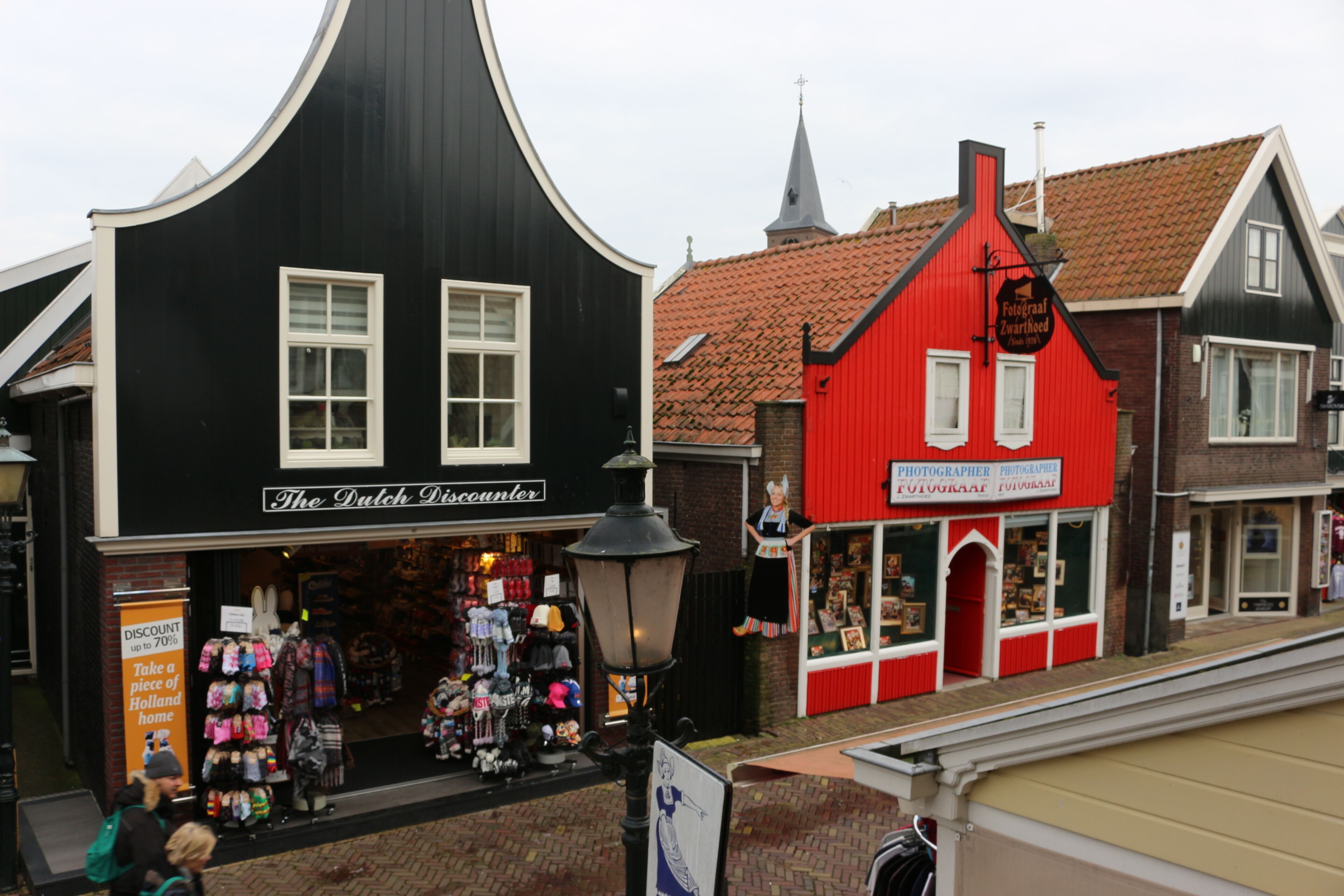 A street view with a black building labeled "The Dutch Discounters" and a red building with a sign "Fotograaf Zwarthed".