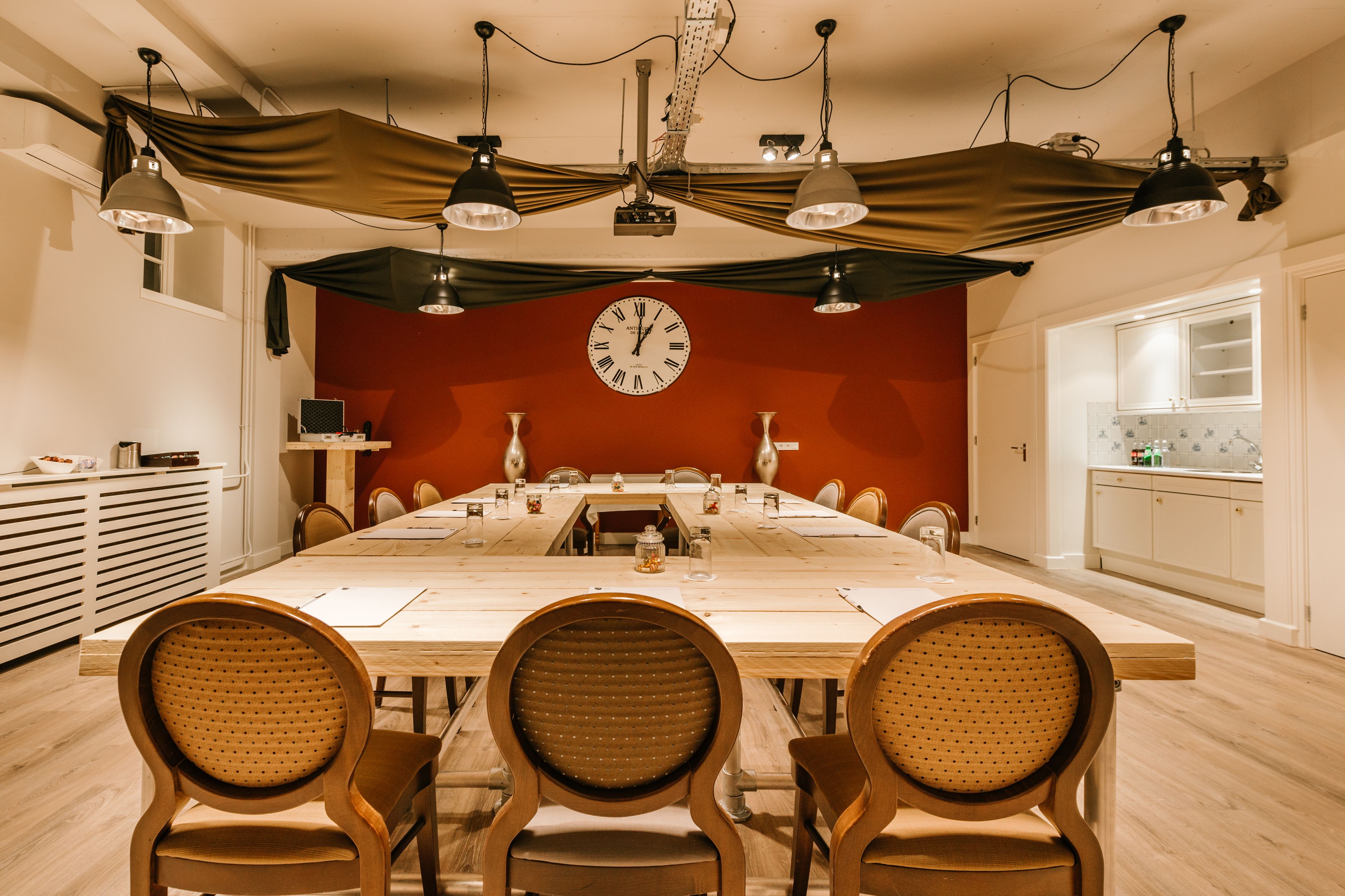 A dining room with a long table, chairs, a clock, and pendant lights.