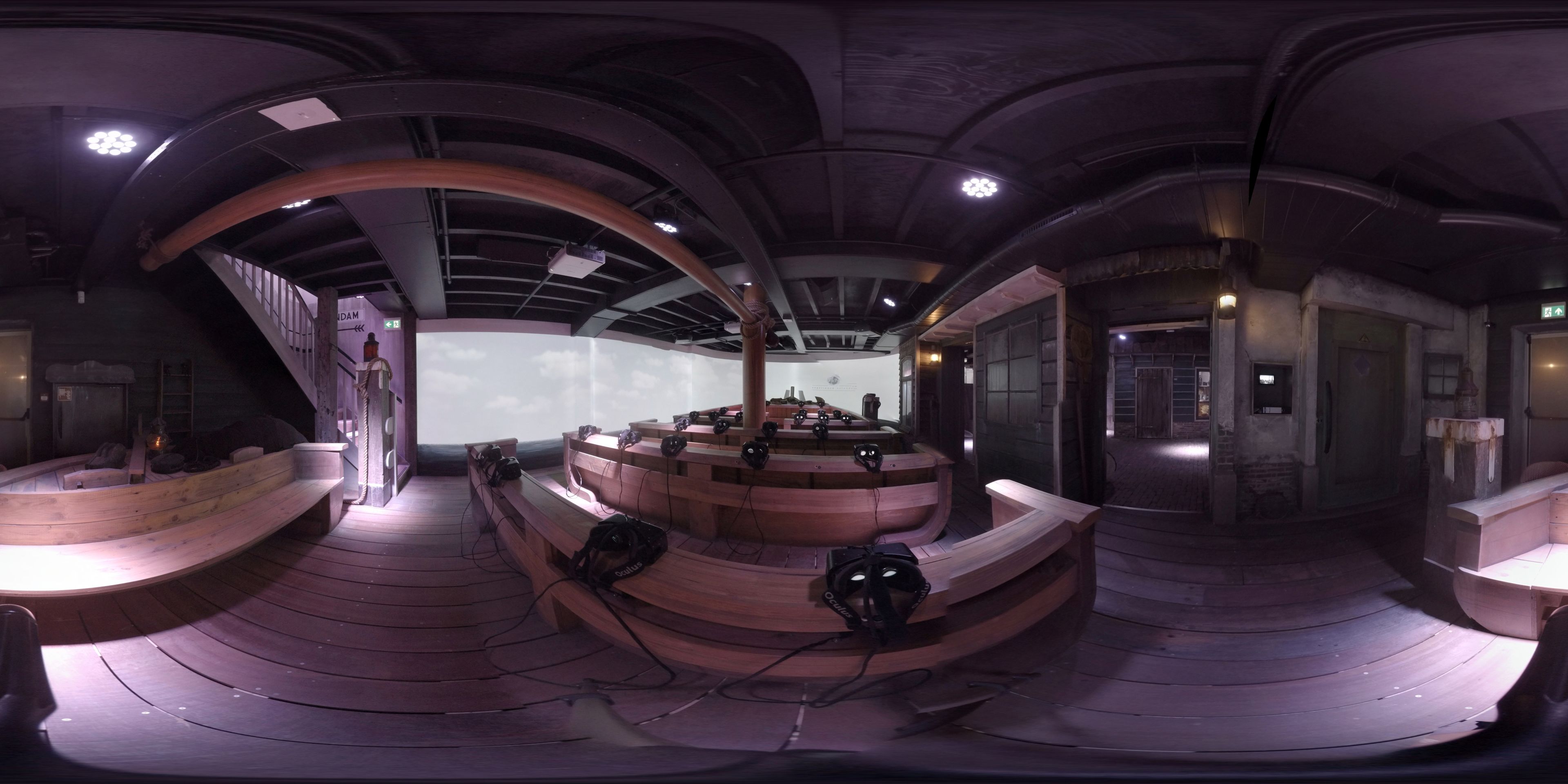A circular room with a central stage, wooden benches, and a projector screen.