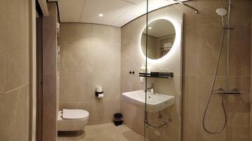 Un baño moderno con ducha de vidrio, un lavabo blanco y un inodoro.