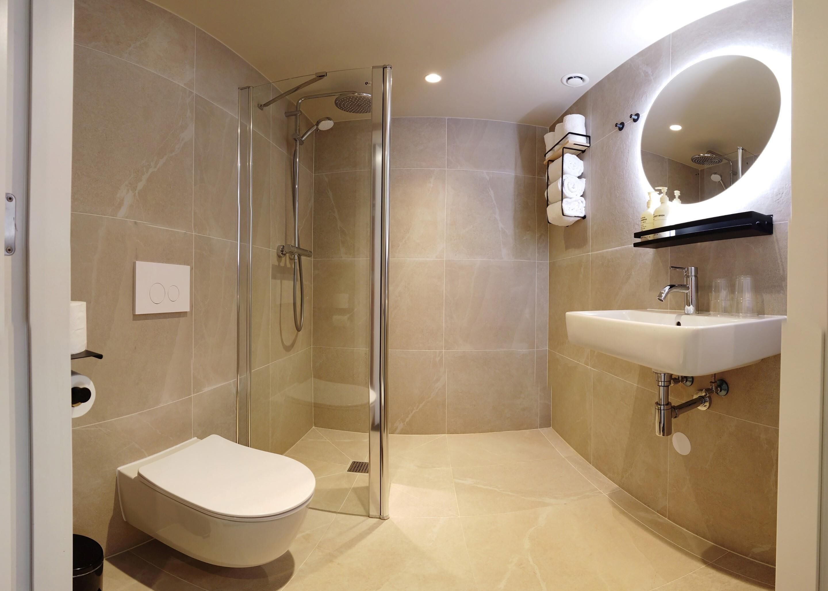 A modern bathroom with a glass-enclosed shower, a toilet, and a sink with a mirror above.