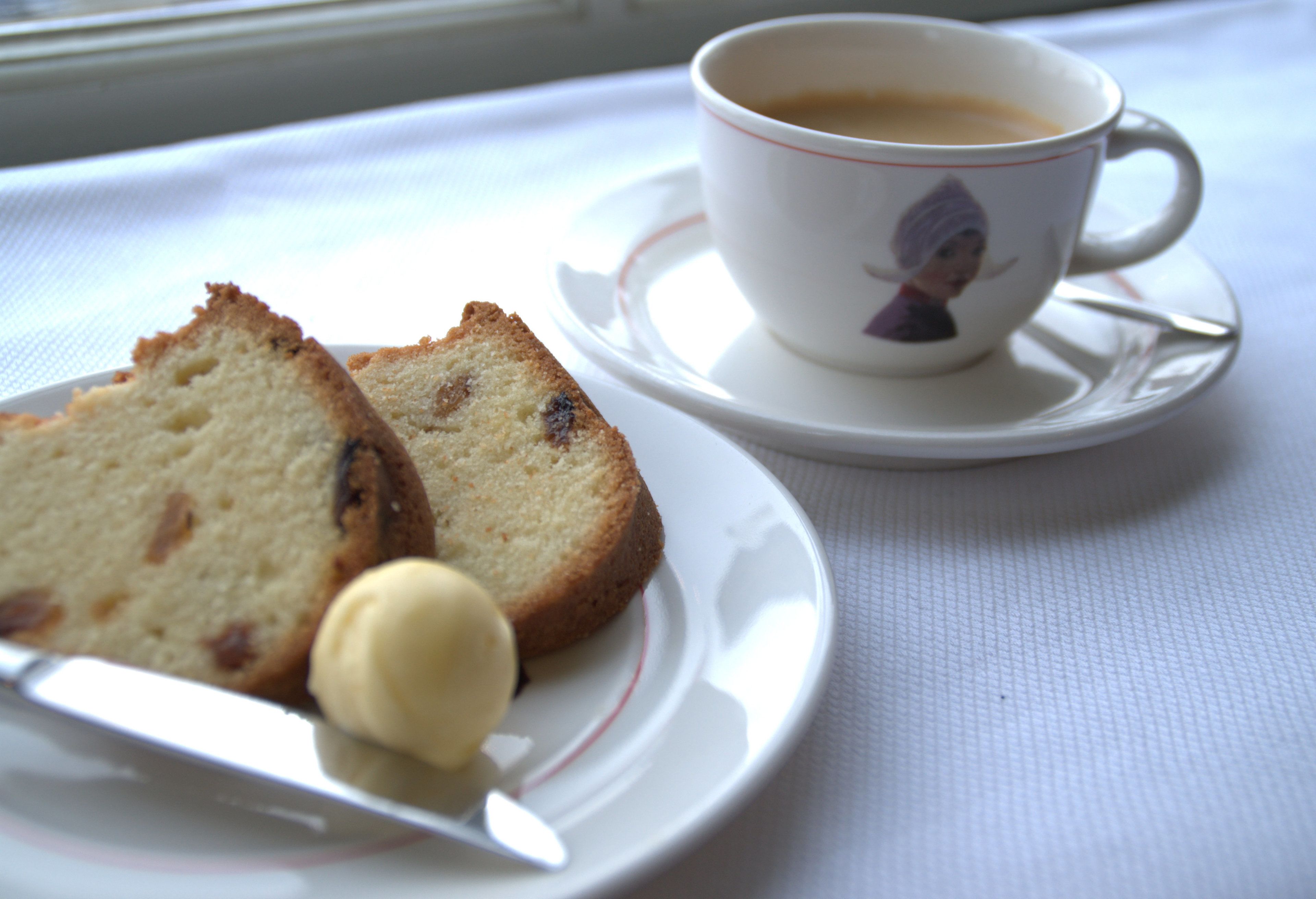 Una rebanada de pastel con una cucharada de crema en un plato, una taza de café y un platillo con una taza.