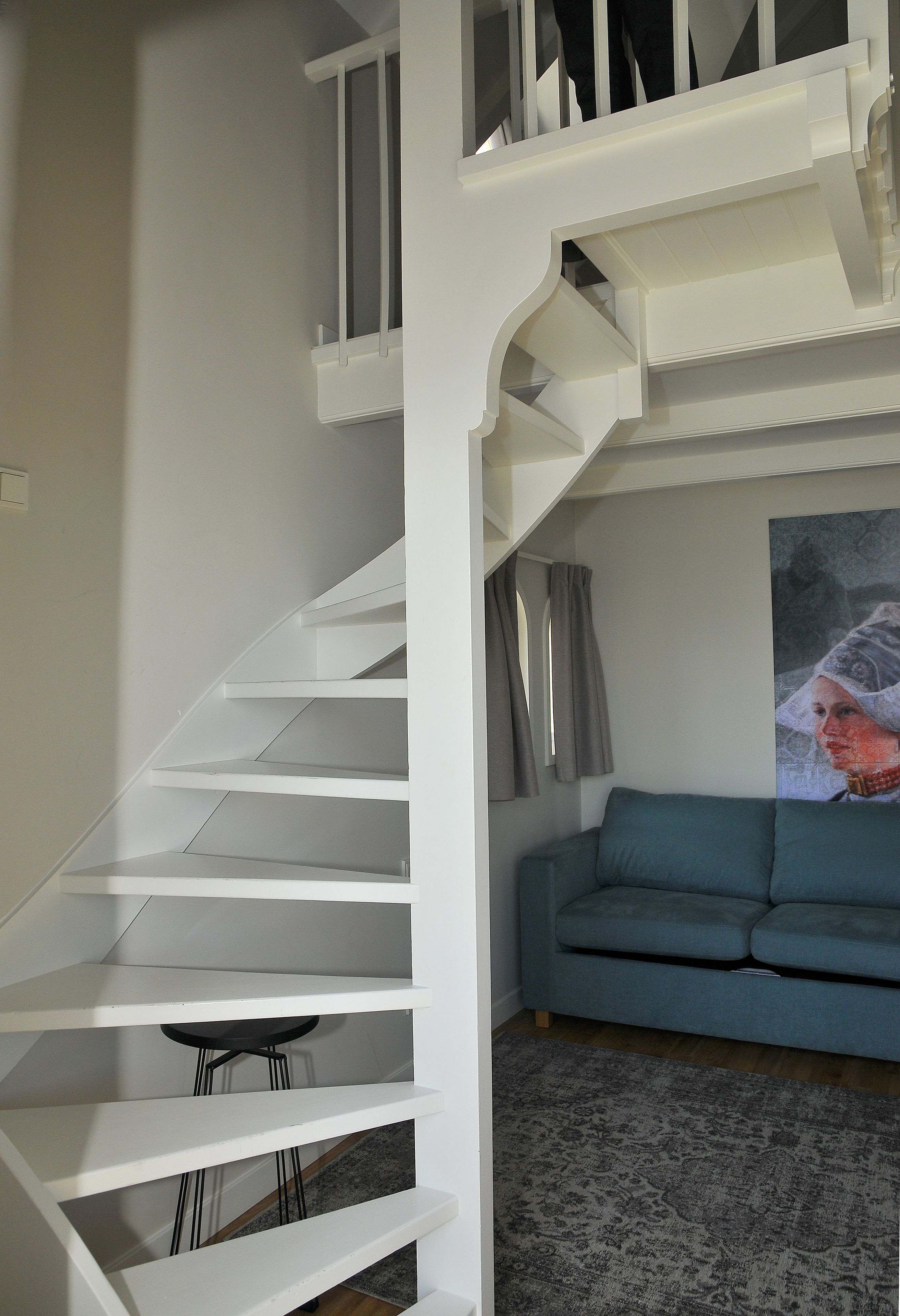 Eine Treppe mit wei ßen Geländern führt zu einer zweiten Etage, dort ein blaues Sofa und ein Teppich mit Muster in einem modernen Interieur.