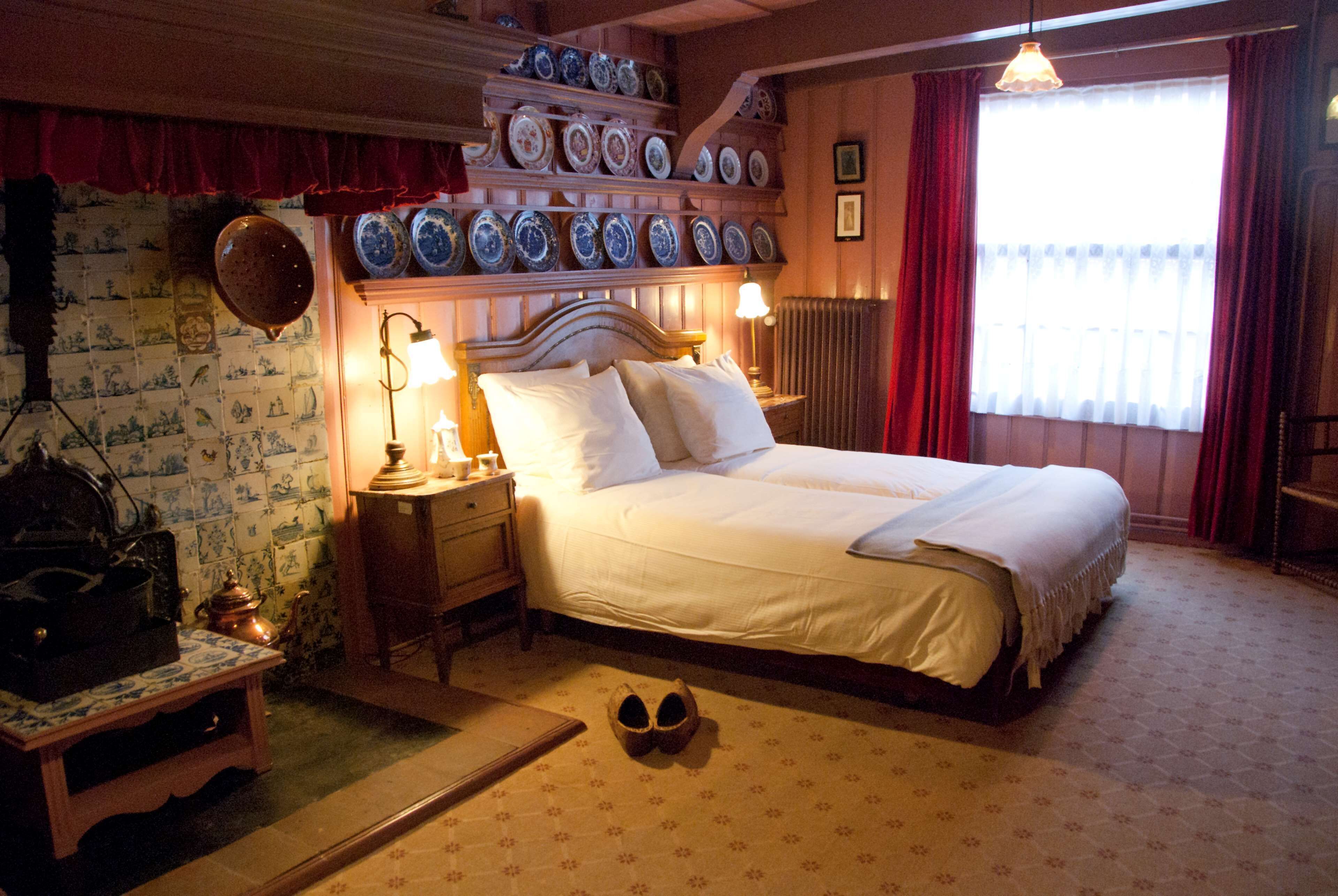 A traditional bedroom with a bed, bedside tables, and a wall of decorative plates.