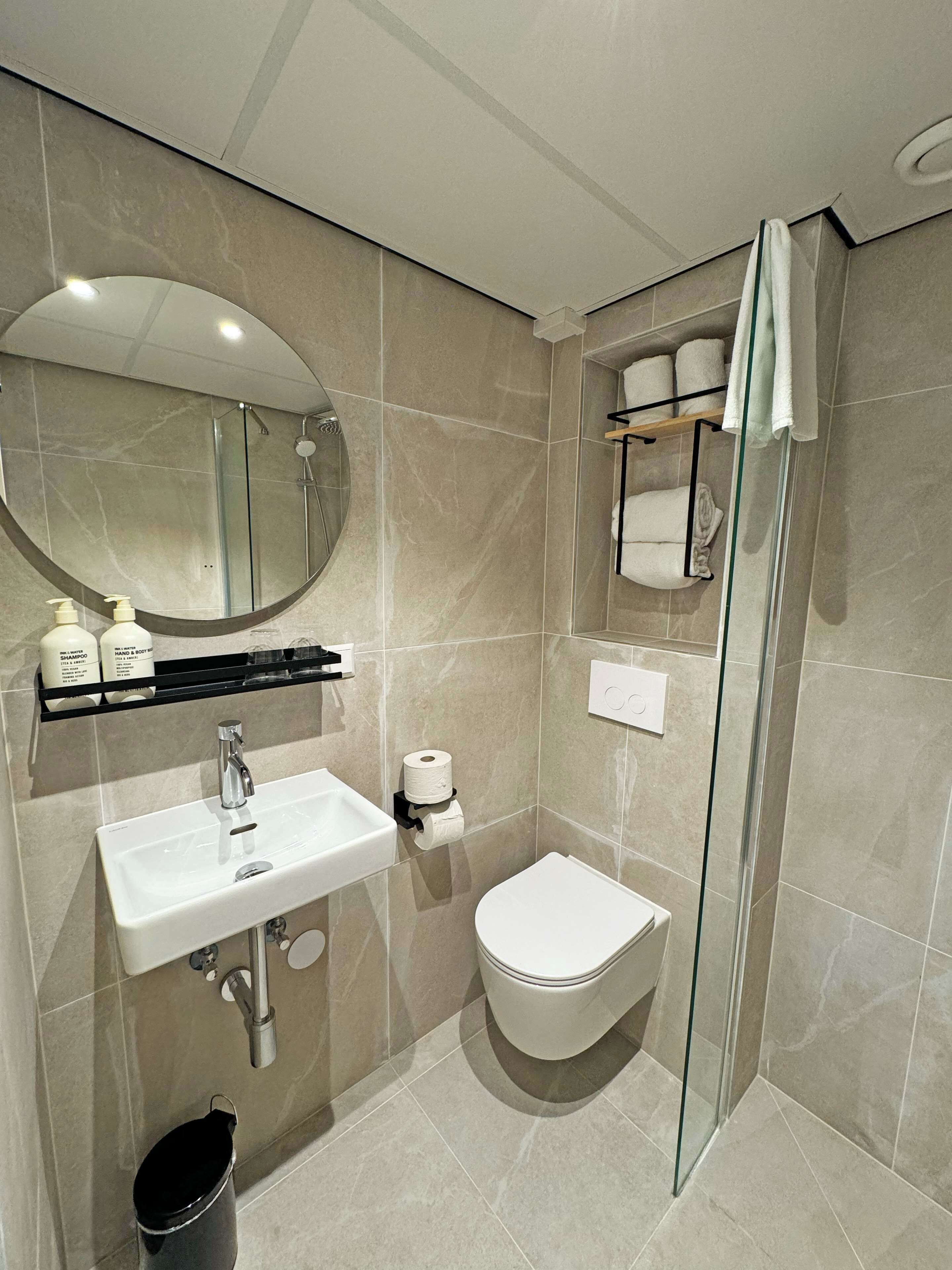 Ein modernes Badezimmer mit rundem Spiegel, Waschbecken, Toilette und einer Duschkabine.