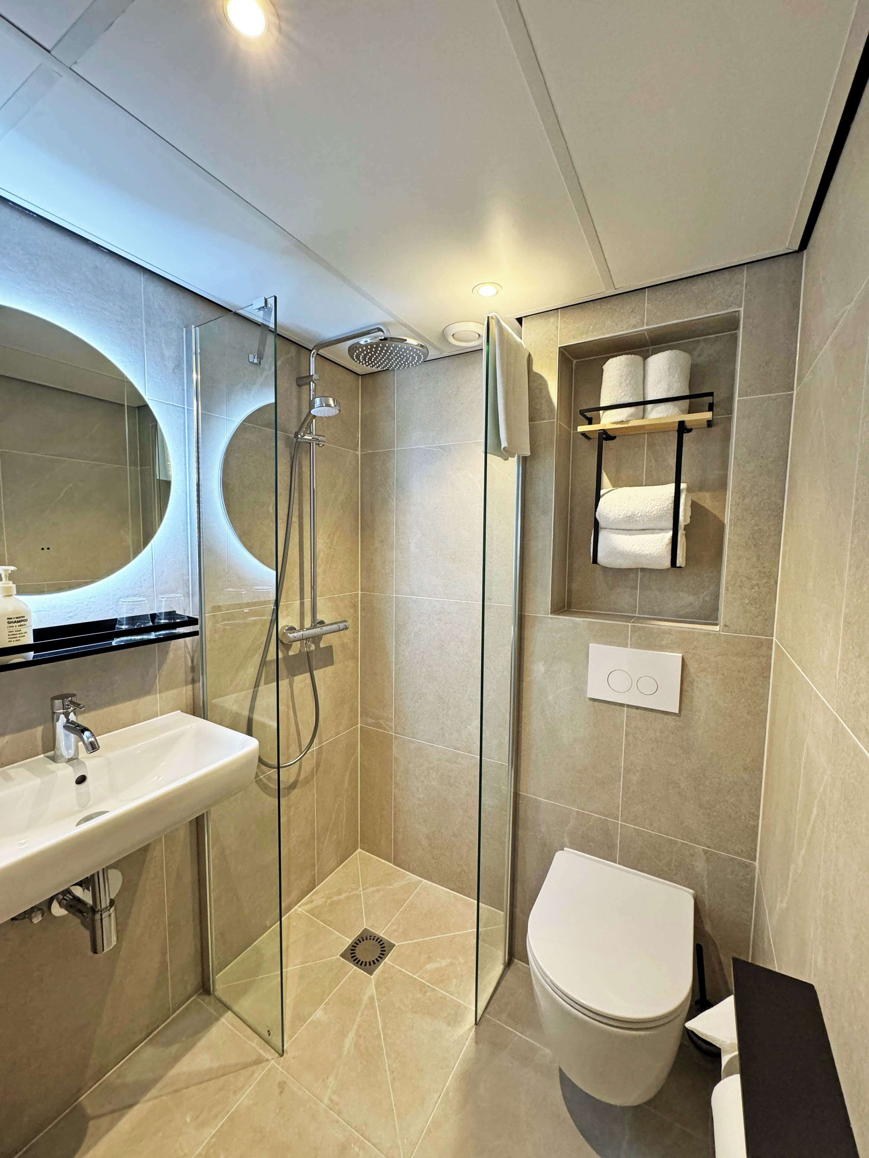 A modern bathroom with a glass-enclosed shower, a sink with a mirror above it, and a toilet.