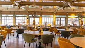 A spacious dining area with multiple round tables and chairs, large windows, and decorative vases. - Hotel Spaander, BW Signature Collection (Volendam)