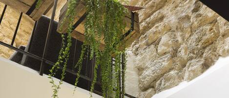 Pared de piedra con hiedra verde colgante en una habitación con techo de madera y una ventana.