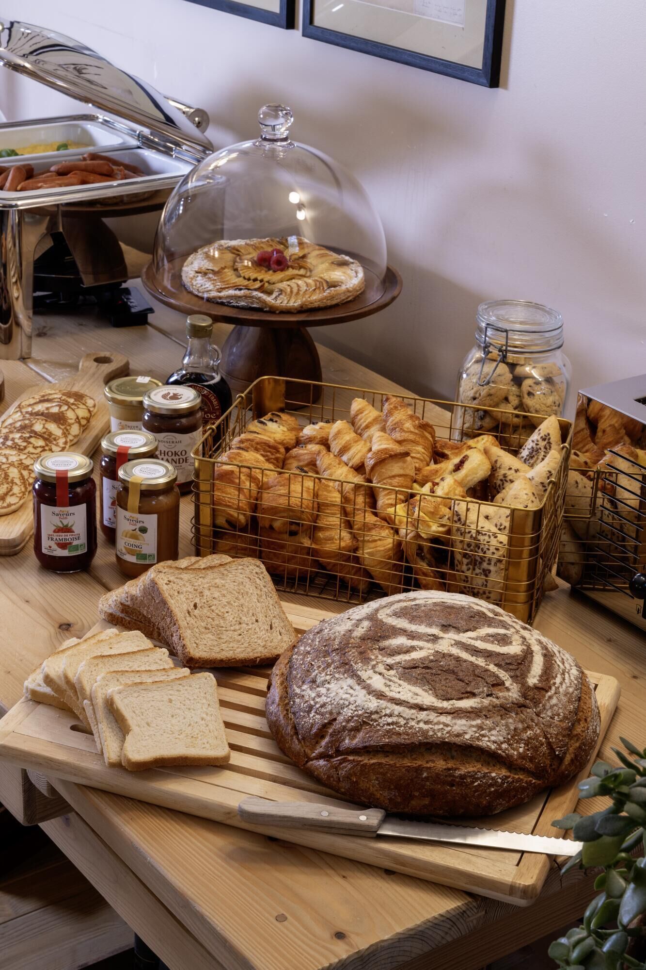 A buffet table with various breads, pastries, and condiments.