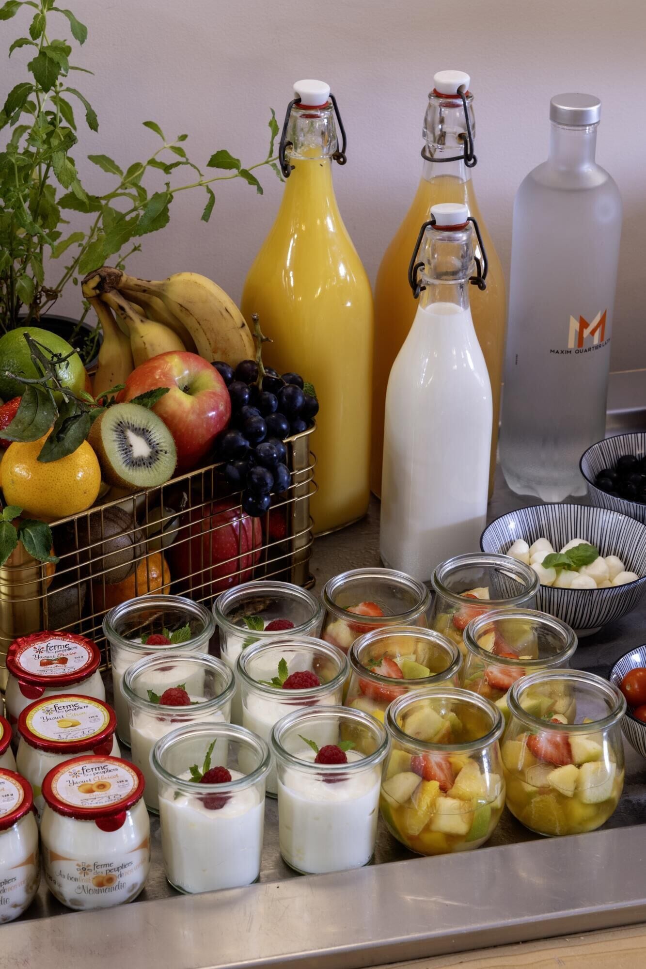 Un bufé de desayuno con diversas frutas, vasos de yogurt y botellas de jugo.