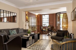 A modern living room with a sofa, armchairs, a coffee table, and a dining area with chairs and a table. - Maxim Quartier Latin (Paris)