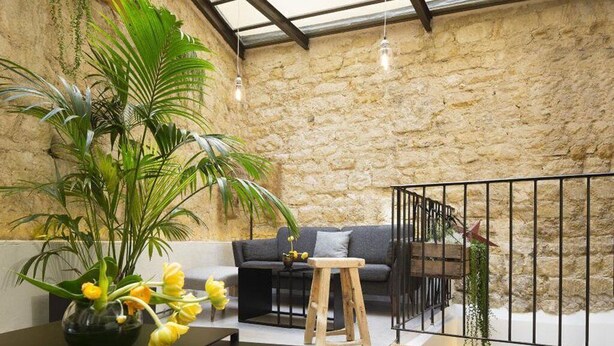 Ein gemütliches Interieur mit Steinwand, einer hölzernen Bank, einer Couch und einem kleinen Tisch mit Blumen.