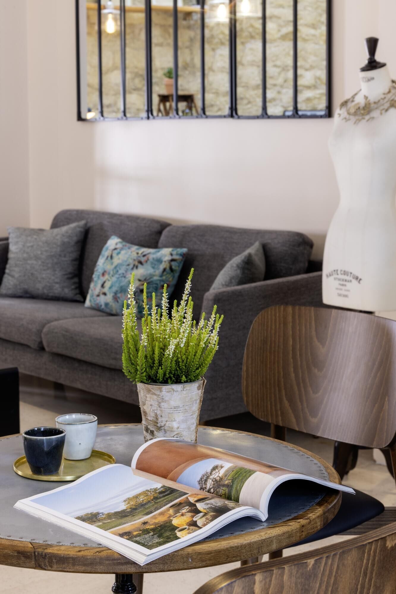 Un salon avec un canapé gris, une plante en pot, un magazine et une table en bois.