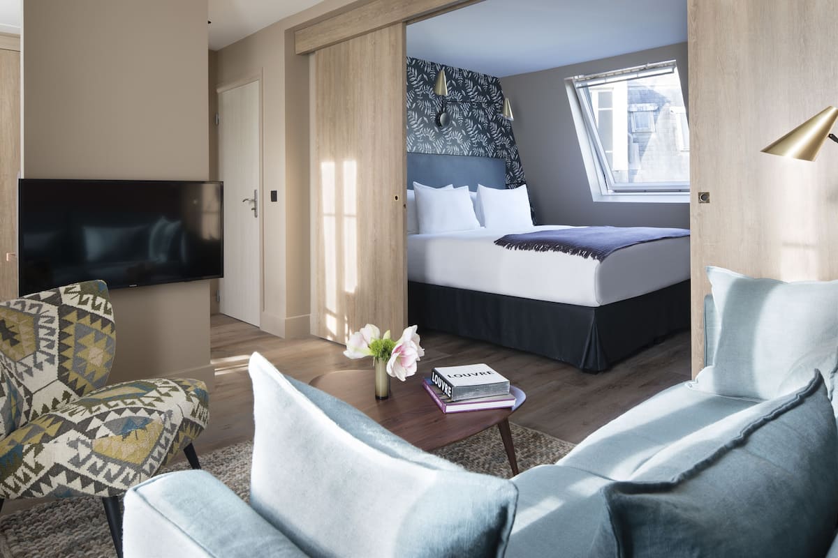 A modern hotel room with a large bed, a TV, a sofa, and a desk with a vase of flowers.