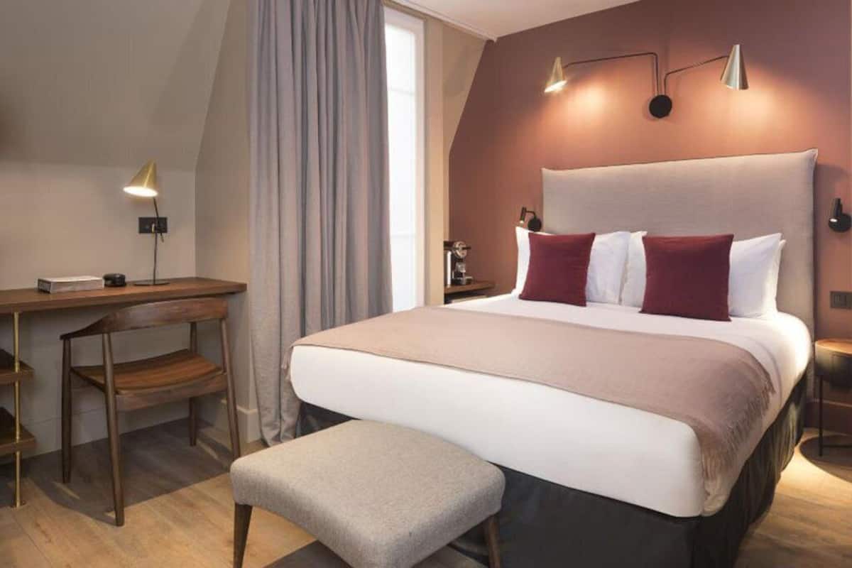 A hotel room with a large bed, a desk, a chair, and a bench.