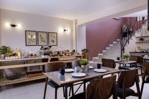 A modern dining area with a long counter, multiple tables, and chairs. There is a staircase with a metal railing leading to an upper level. - Maxim Quartier Latin (Paris)