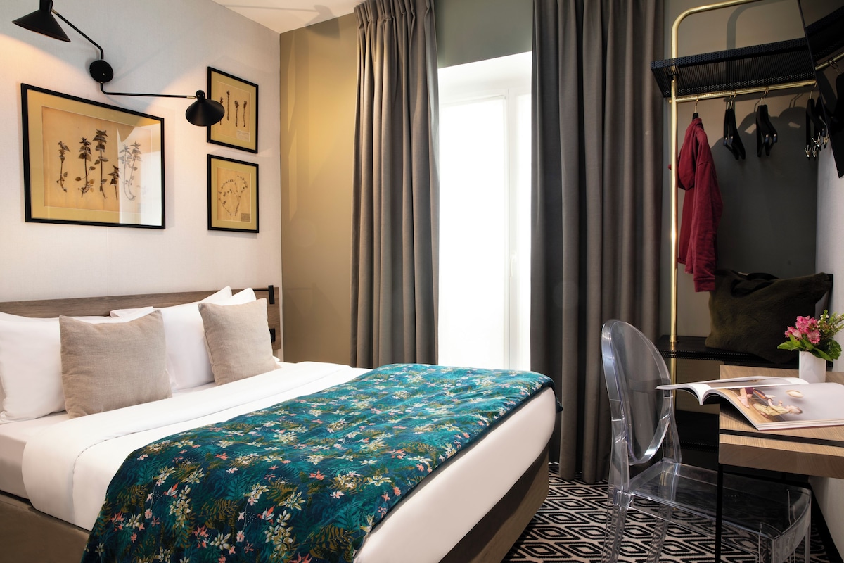 Una habitación de hotel con una cama, un escritorio con silla, un espejo y una ventana con cortinas.