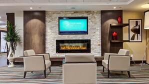 A modern hotel lobby with a stone fireplace, leather armchairs, and a flat-screen TV displaying a contact number. - Best Western Plus Port O'Call Hotel (Calgary)