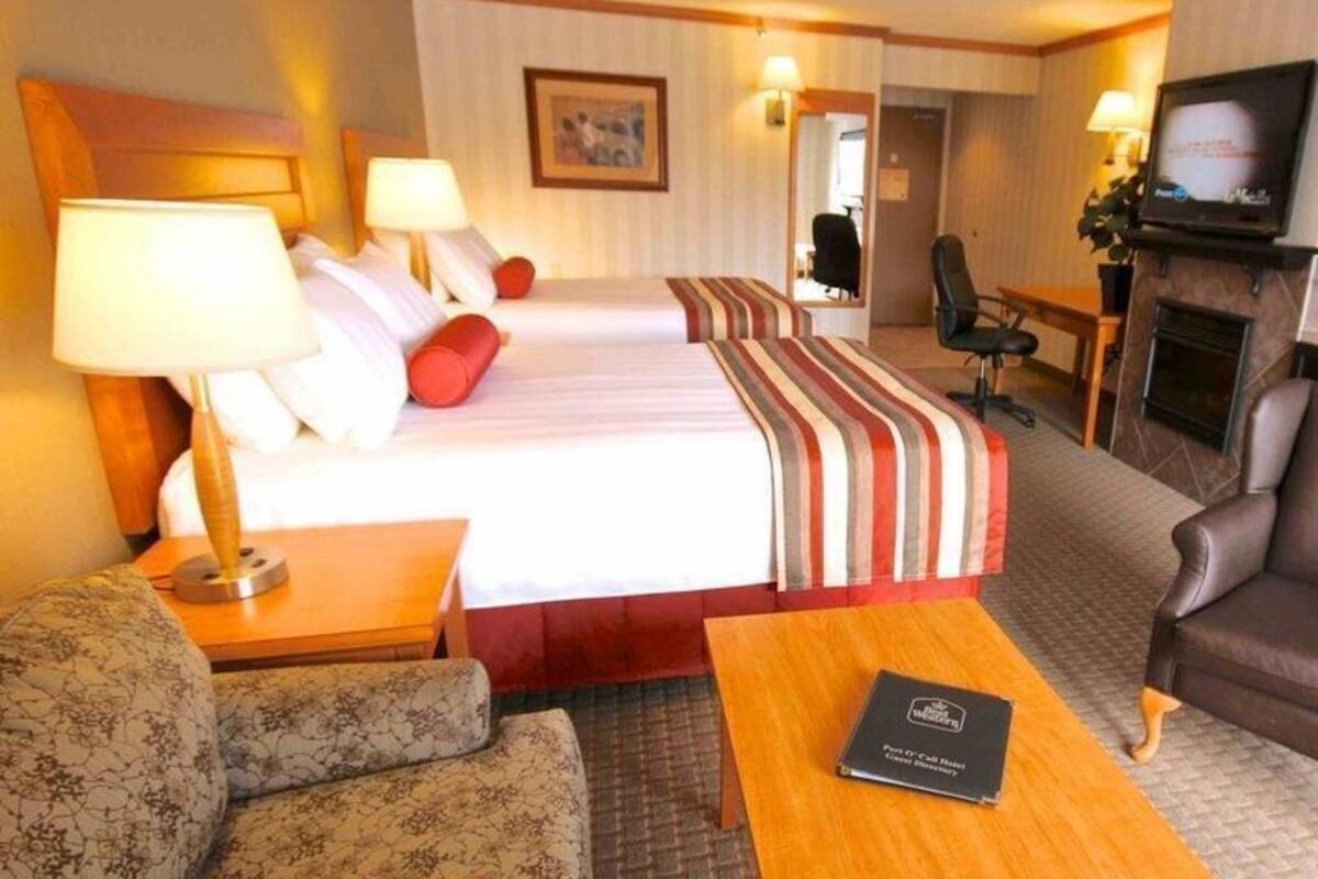 A hotel room with two beds, a sofa, a coffee table, a TV, and a fireplace.