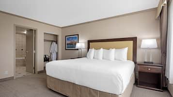 Habitación de hotel con una cama grande, dos lámparas de noche, una mesita de noche, un cuadro en la pared y un baño visible a través de una puerta abierta.