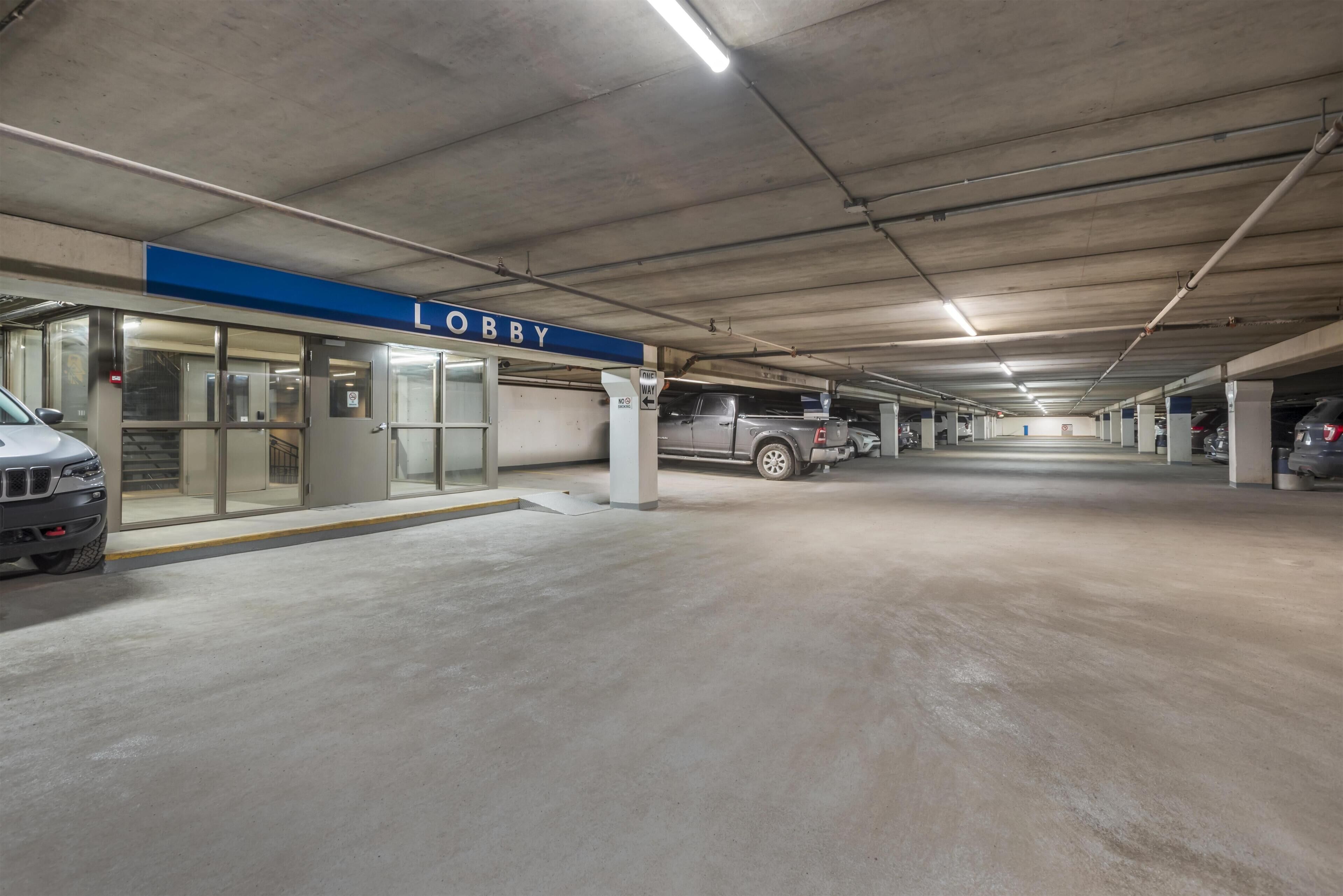 Un parking à plusieurs niveaux, avec une pancarte indiquant « Hall d’entrée », des planchers en béton et plusieurs véhicules stationnés.