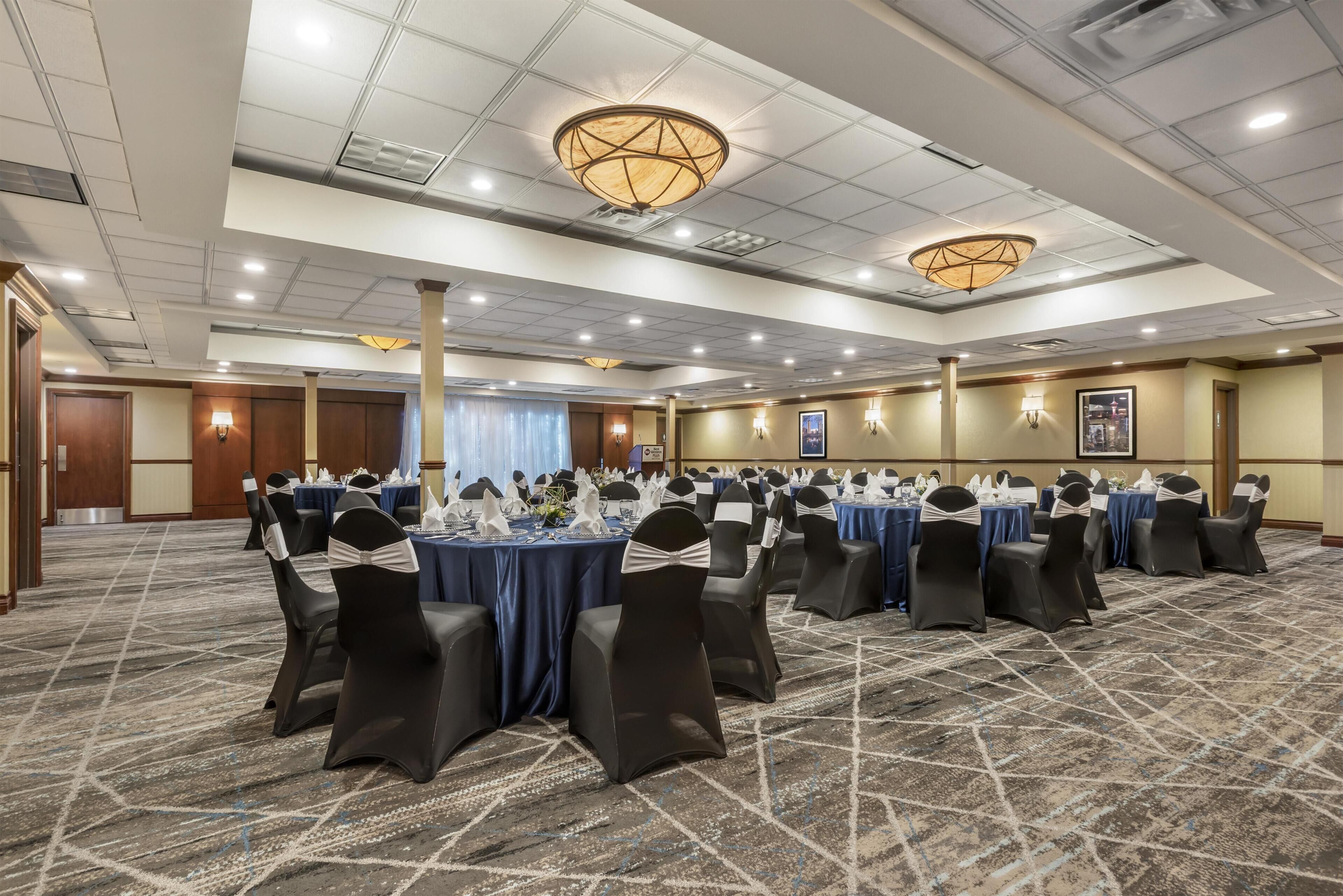 A conference room with tables set for a meeting, black chairs with sashes, and a patterned carpet.