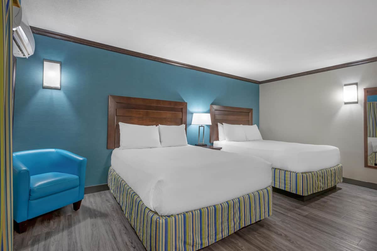 A hotel room with two beds, a blue armchair, and a wooden headboard.