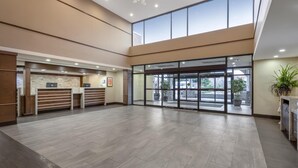 A spacious lobby with a reception desk, a large glass door entrance, and a ceiling light fixture. - Best Western Plus Port O'Call Hotel (Calgary)