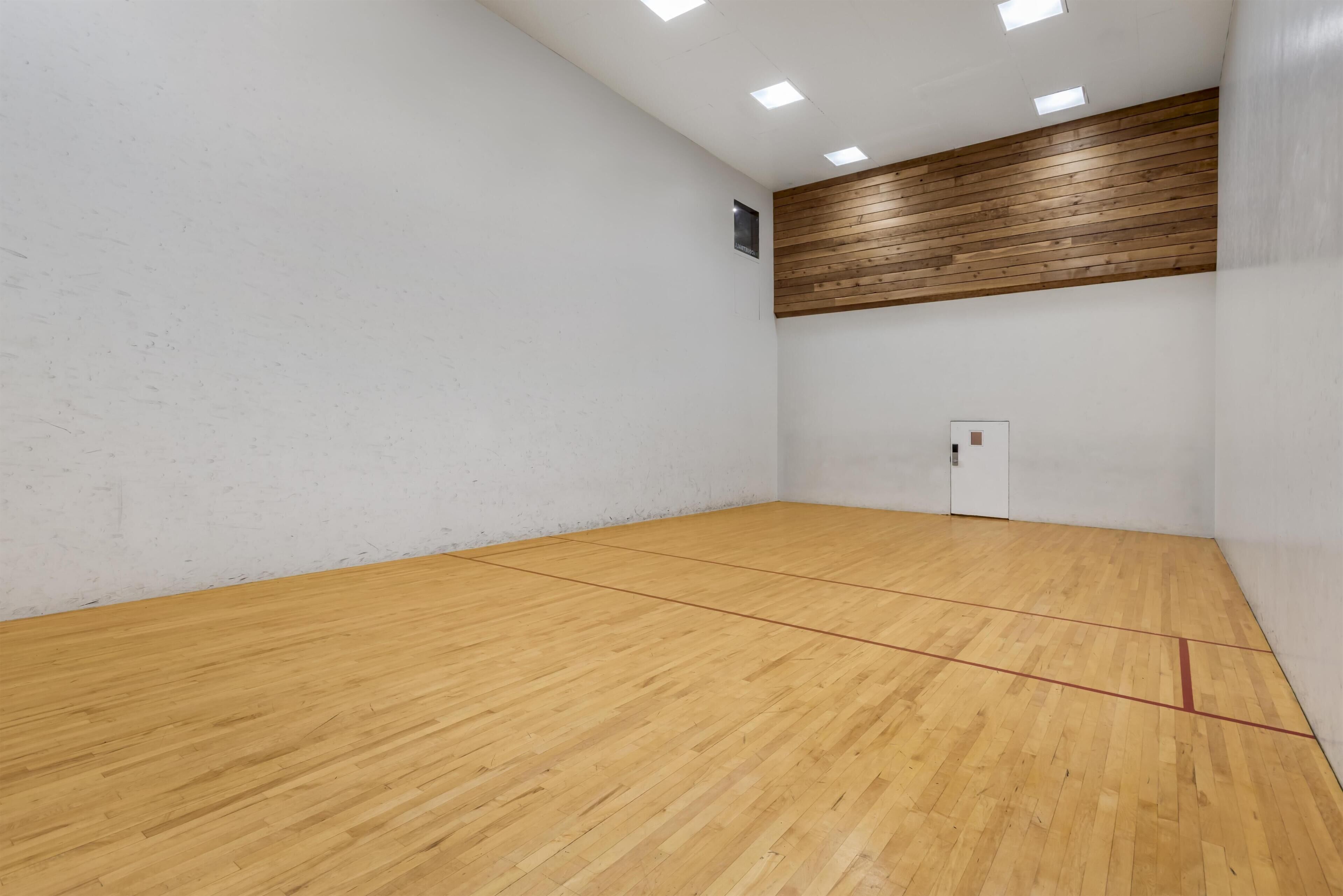 A squash court with wooden flooring, white walls, and a wooden panel ceiling.