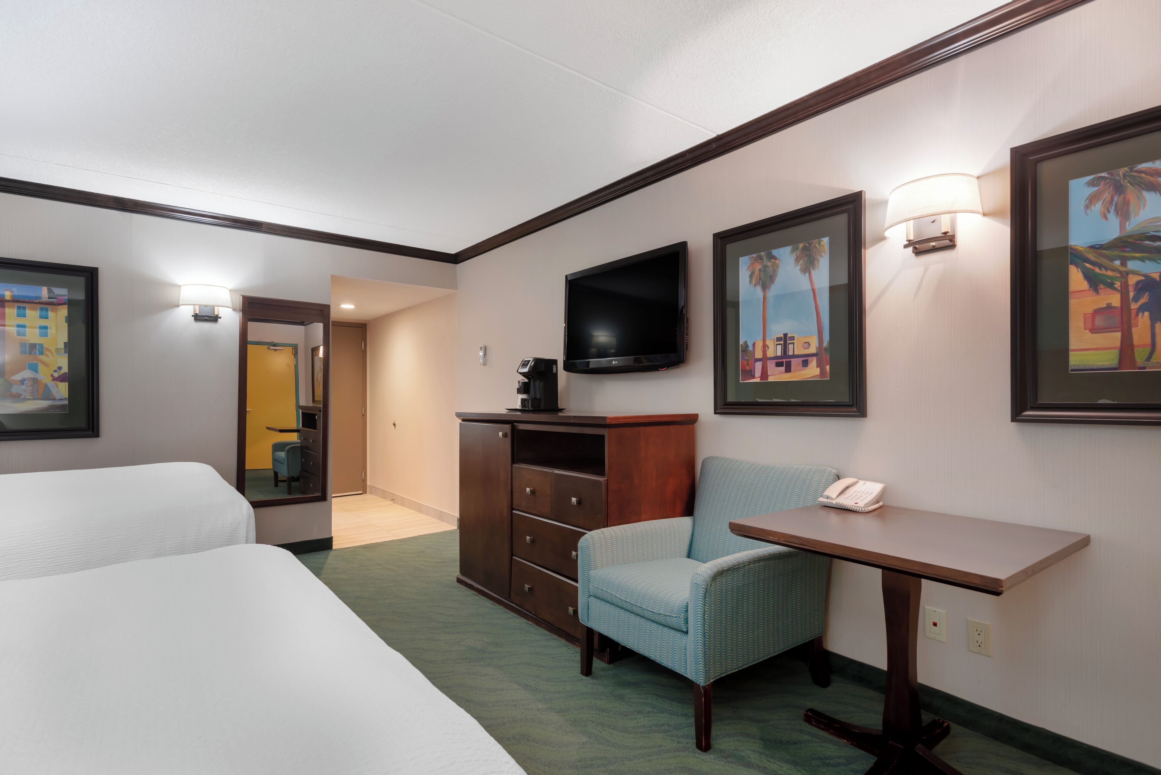 Een hotelkamer met twee bedden, een bureau met telefoon, een televisie en lijstjes met kunstwerken aan de muren.