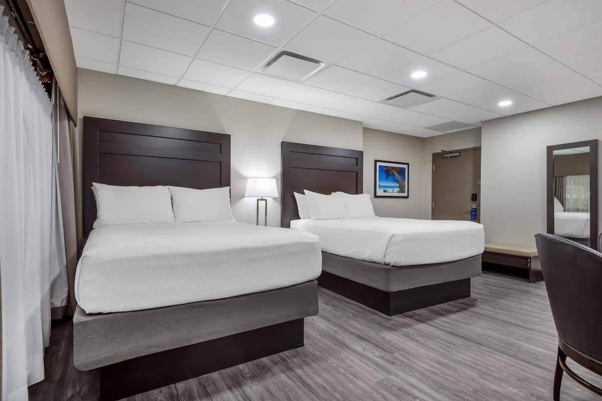 A hotel room with two beds, a desk, a chair, a lamp, a picture on the wall, and a ceiling light.