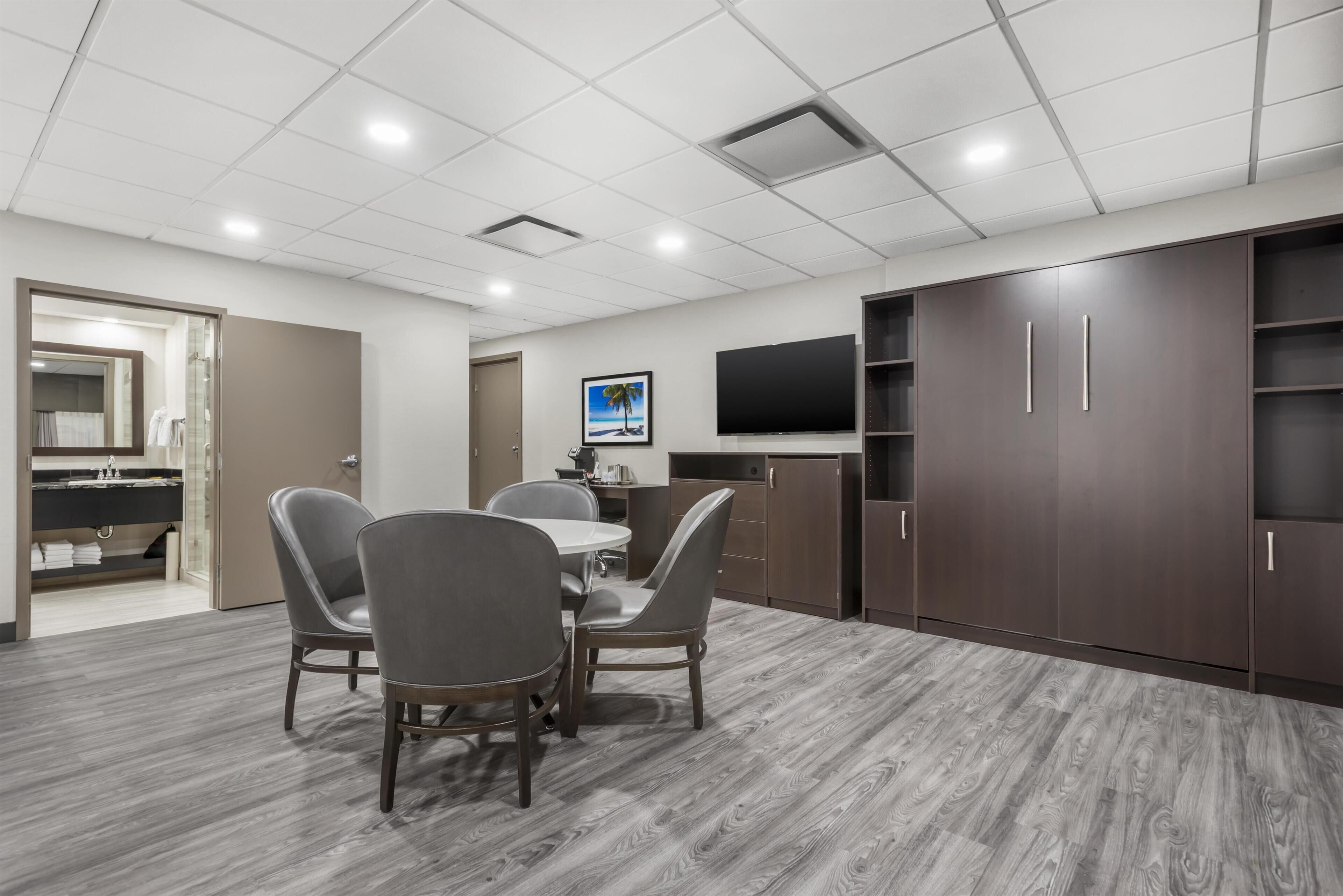 A modern conference room with a round table, two chairs, a television, and a large cabinet.