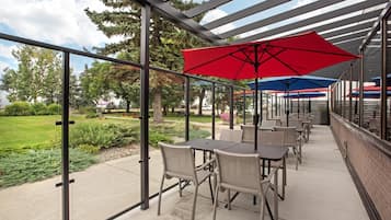 Un patio al aire libre con mesas y sillas, cubierto por una pérgola de metal con sombrillas rojas y azules.