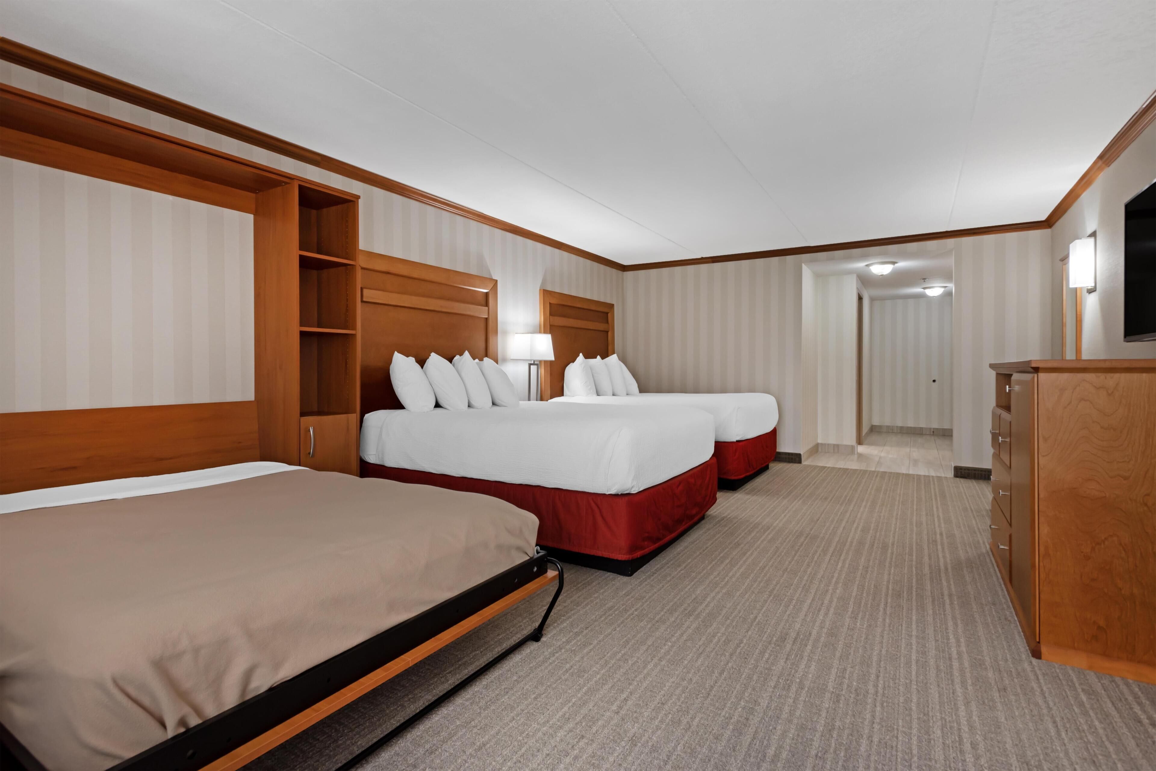 A hotel room with two beds, a wardrobe, a desk, and a lamp.