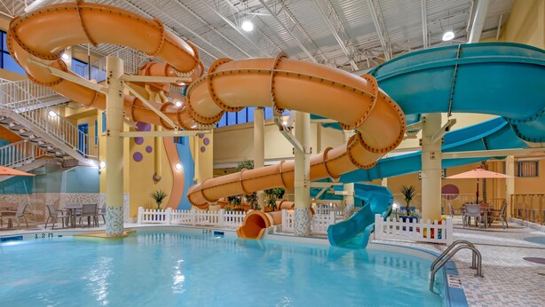 An indoor swimming pool with multiple water slides, a staircase, and a seating area with tables and chairs. - Best Western Plus Port O'Call Hotel (Calgary)