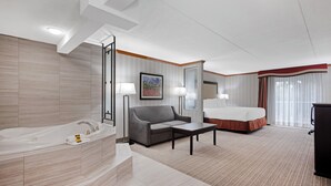 A hotel room with a large bathtub, a gray sofa, a small table, a bed, and a television. - Best Western Plus Port O'Call Hotel (Calgary)