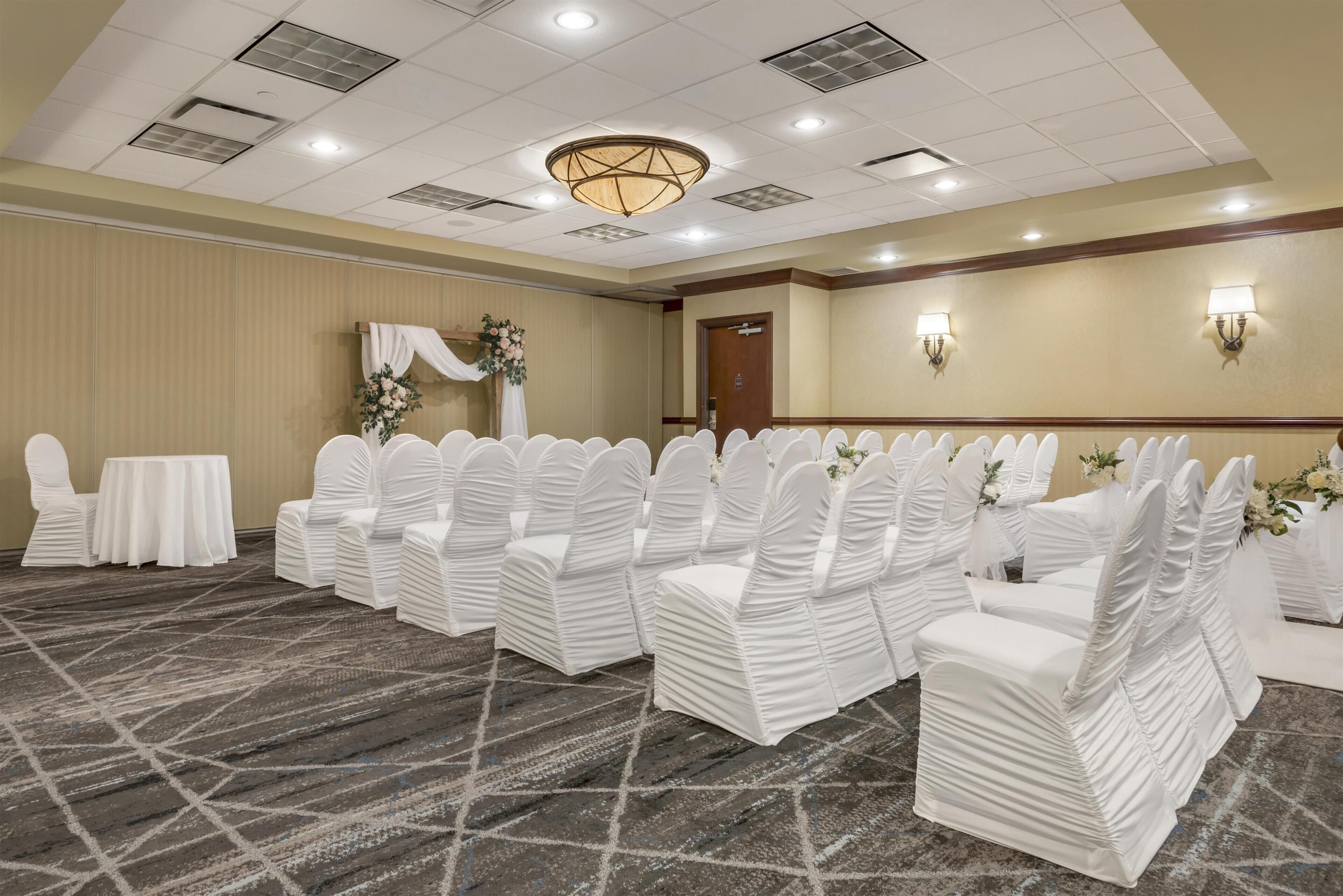A conference room with rows of white chairs, a table, and a floral arrangement.