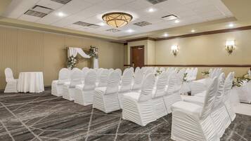 A conference room with rows of white chairs, a table, and a floral arrangement.