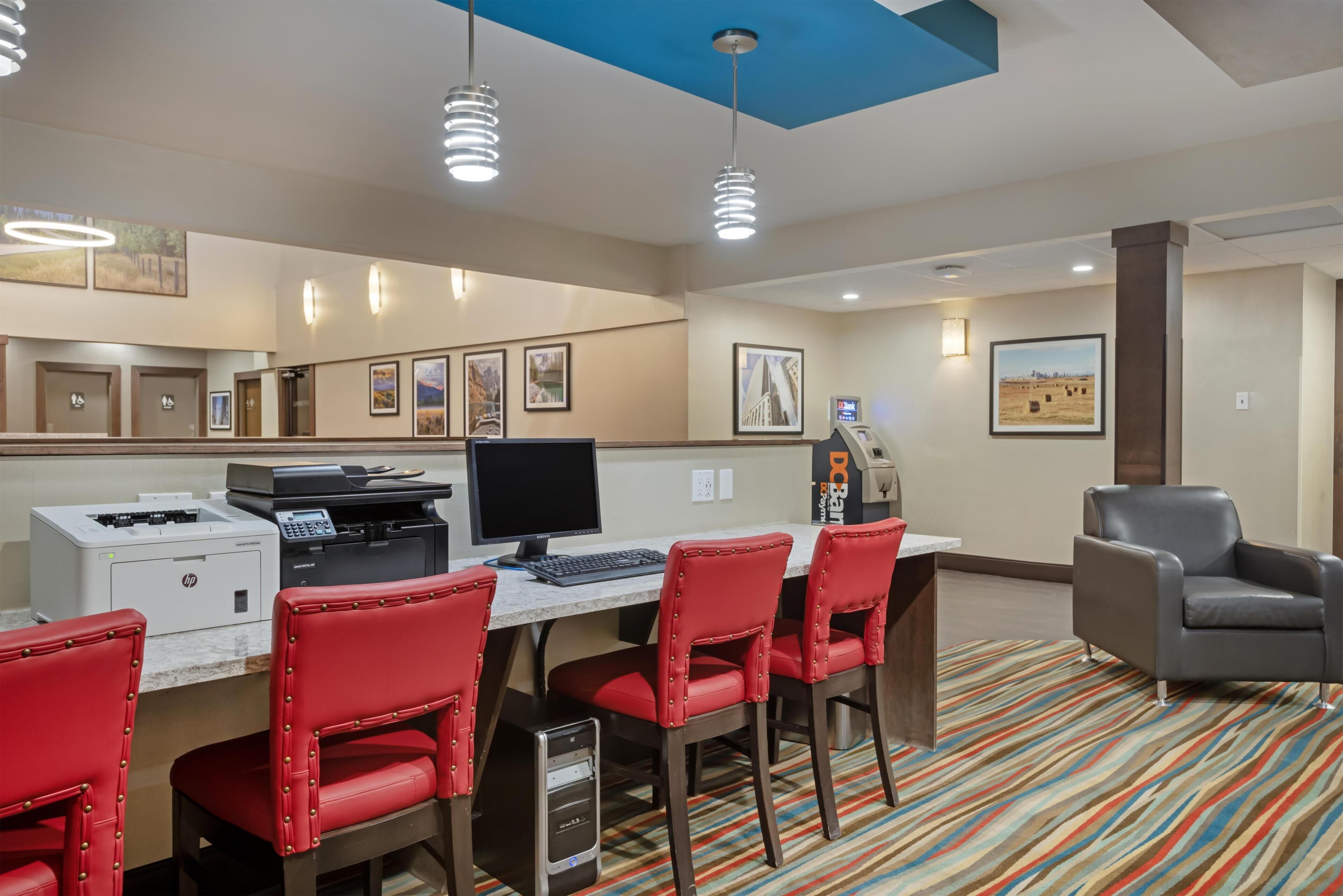 Una habitación de hotel con escritorio, computadora, impresora y sillas rojas.