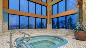A large indoor swimming pool with clear views through large windows, a tiled floor, and a metal pool ladder. - Best Western Plus Port O'Call Hotel (Calgary)