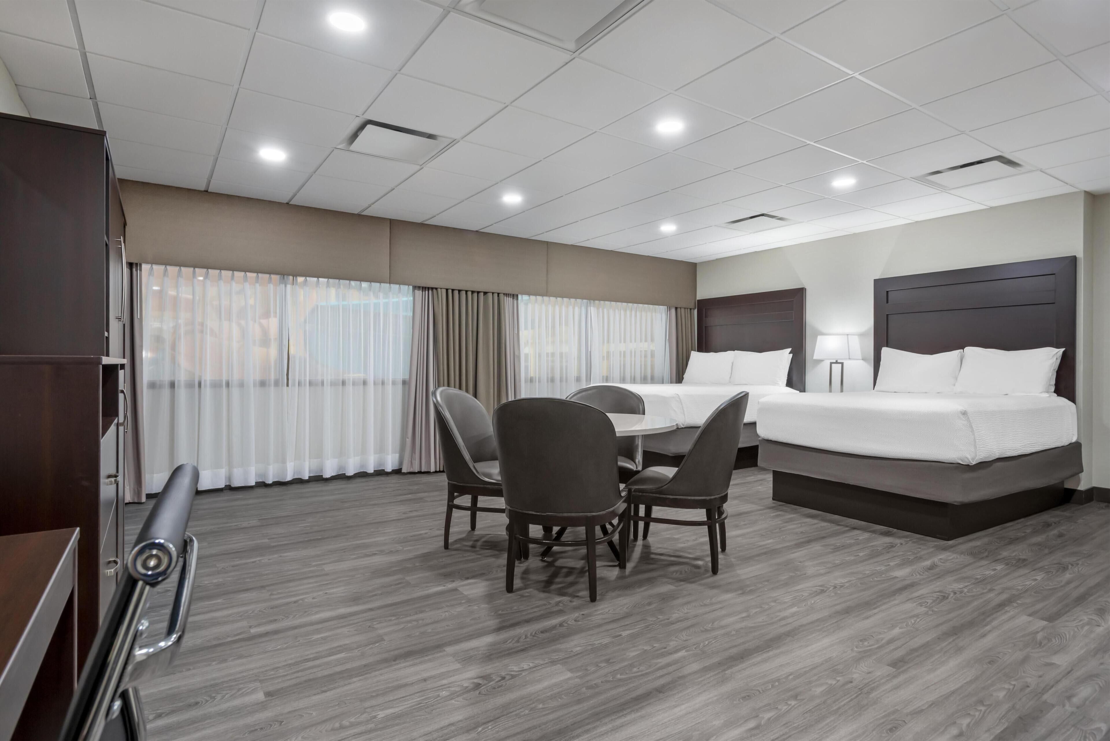 A hotel room with a bed, a desk, a chair, a table, and a window with curtains.