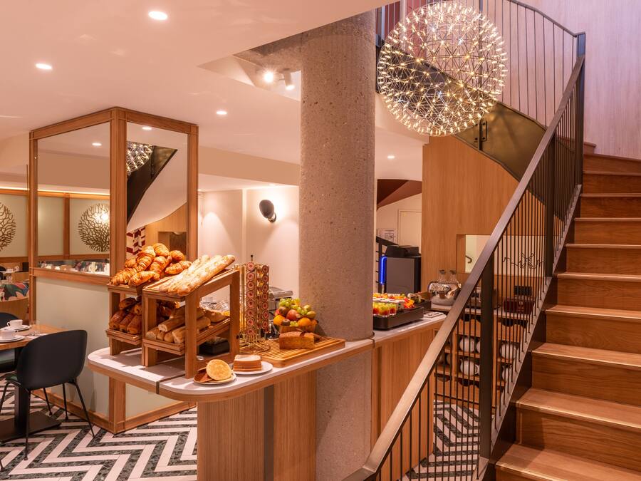 Un interior moderno con una escalera de madera, un mostrador de buffet con pasteles y frutas, y una lámpara esférica decorativa.